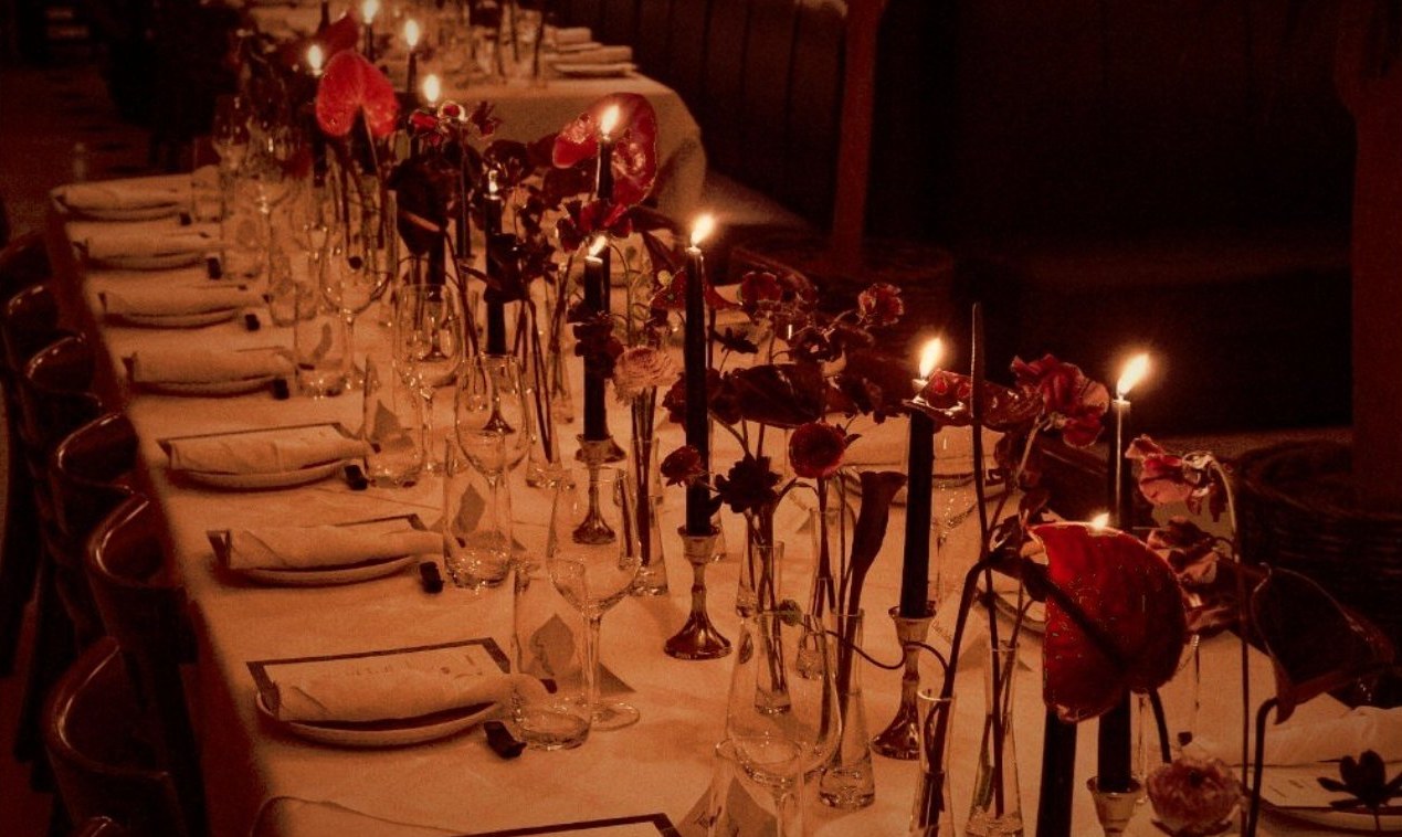 Candlelit long table set for a private dinner with red anthurium florals